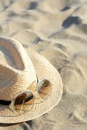 Photo of Hat with beautiful sunglasses on sand near sea. Space for text
