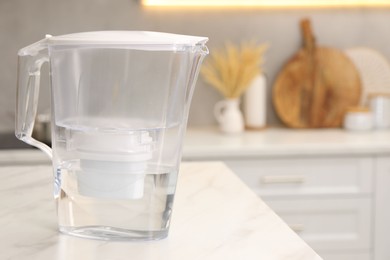 Photo of Water filter jug on white marble table in kitchen, space for text