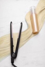 Photo of Spray bottle with thermal protection, lockblonde hair and modern straightener on white marble table, flat lay
