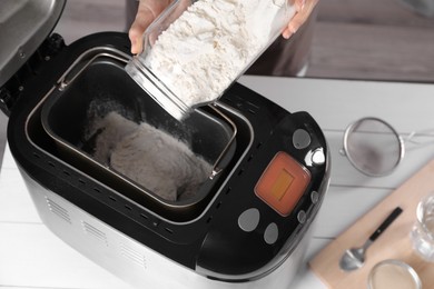 Photo of Woman adding flour into breadmaker at white wooden table indoors, above view