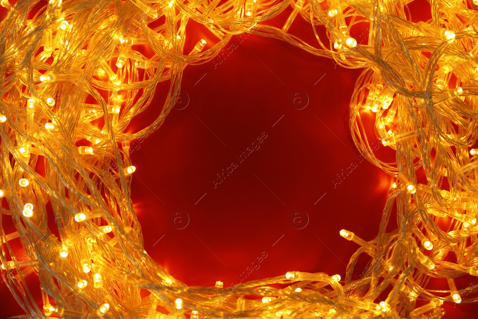 Photo of Frame made of glowing Christmas lights on red background, top view. Space for text