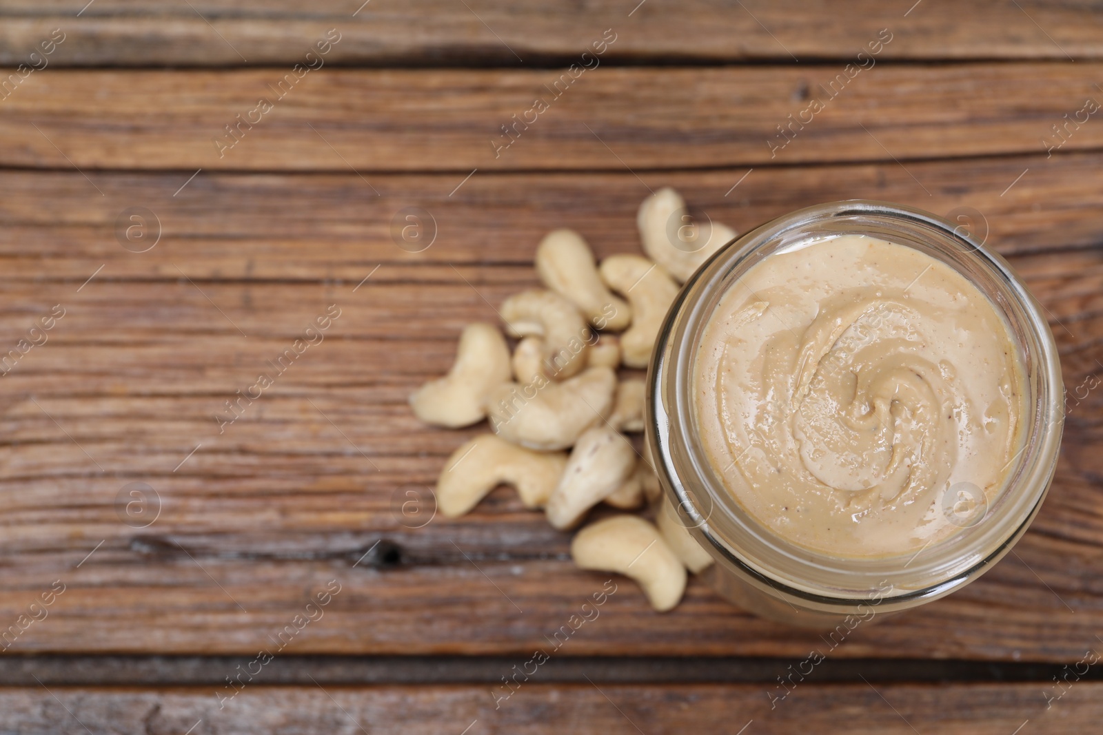 Photo of Tasty cashew nut paste in jar on wooden table, top view. Space for text