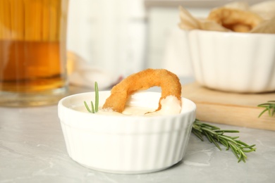 Photo of Delicious crunchy fried onion ring in bowl with sauce on grey marble table