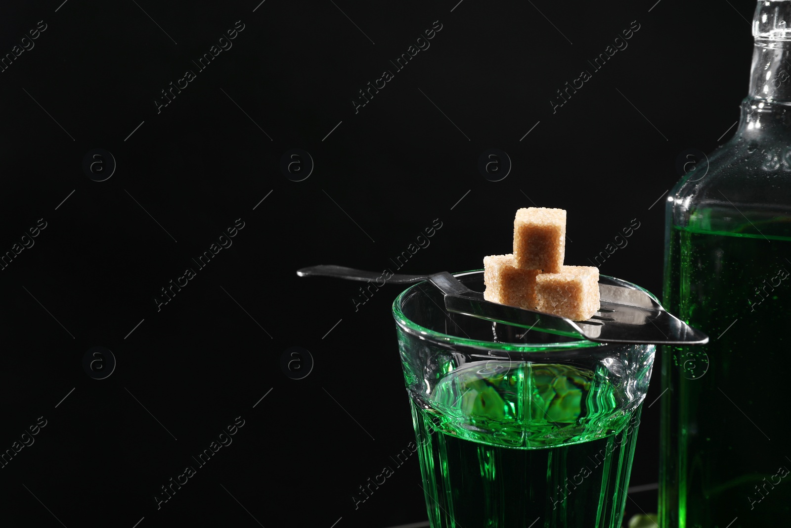 Photo of Absinthe in glass, brown sugar and spoon against black background, space for text. Alcoholic drink