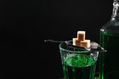 Photo of Absinthe in glass, brown sugar and spoon against black background, space for text. Alcoholic drink