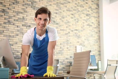 Young man in apron and gloves cleaning office