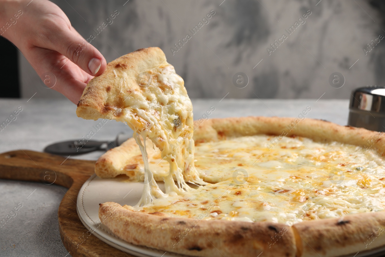 Photo of Woman taking piece of delicious cheese pizza at light grey table, closeup