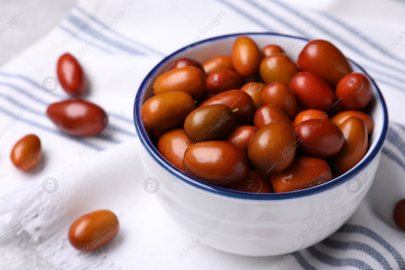 Photo of Fresh Ziziphus jujuba fruits with bowl and napkin on table, closeup