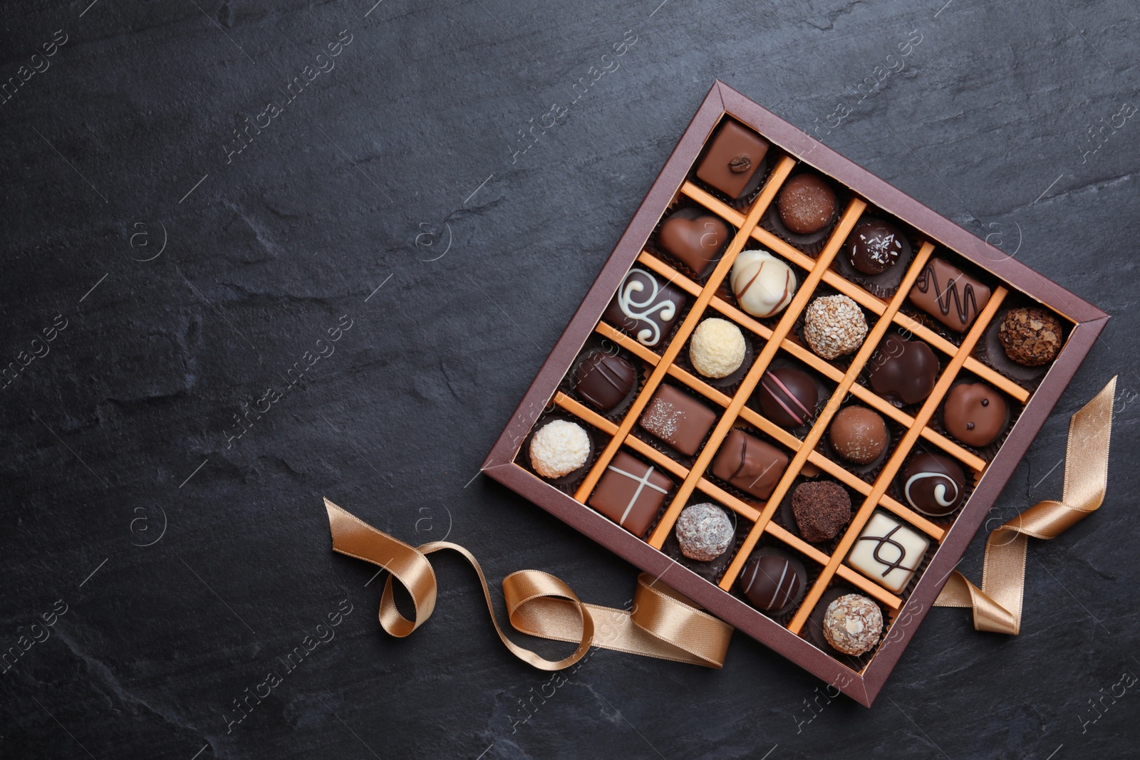 Photo of Box with delicious chocolate candies on black table, flat lay. Space for text