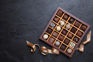 Photo of Box with delicious chocolate candies on black table, flat lay. Space for text