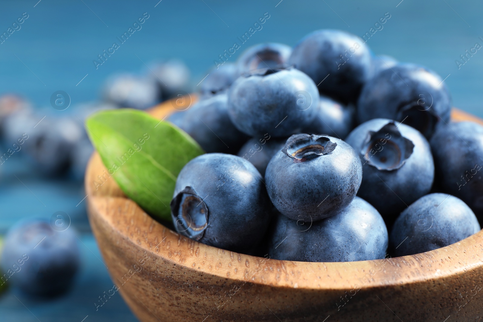 Photo of Bowl of fresh tasty blueberries on blue table, closeup