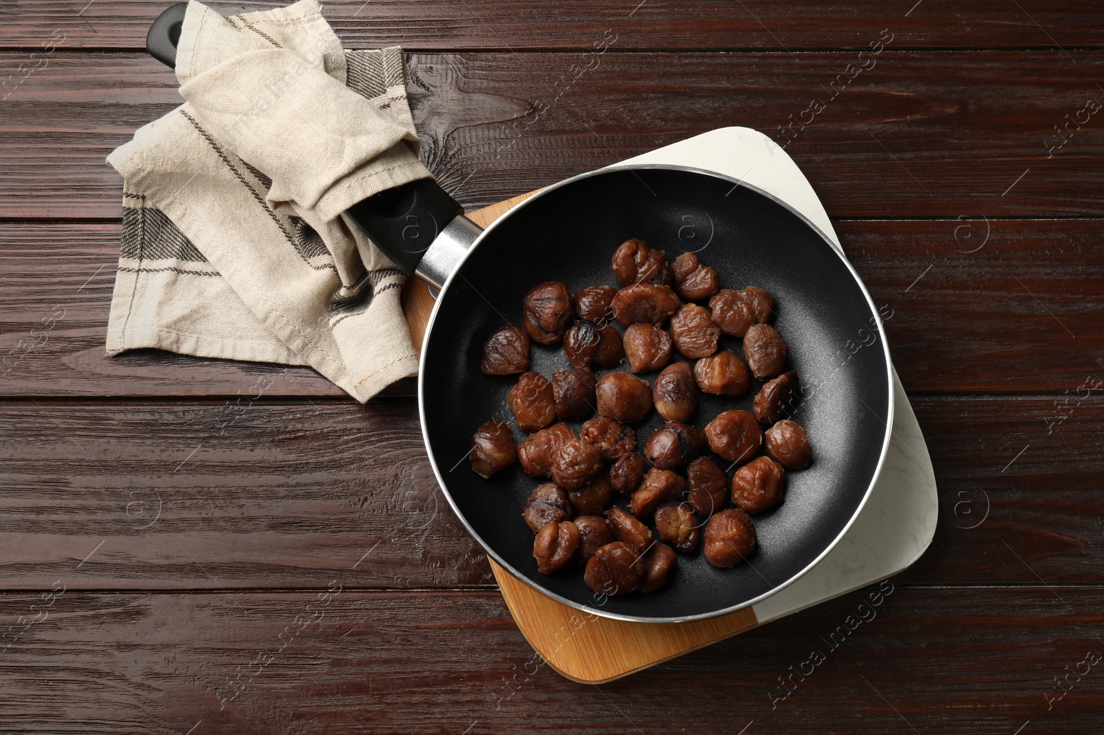 Photo of Roasted edible sweet chestnuts in frying pan on wooden table, top view