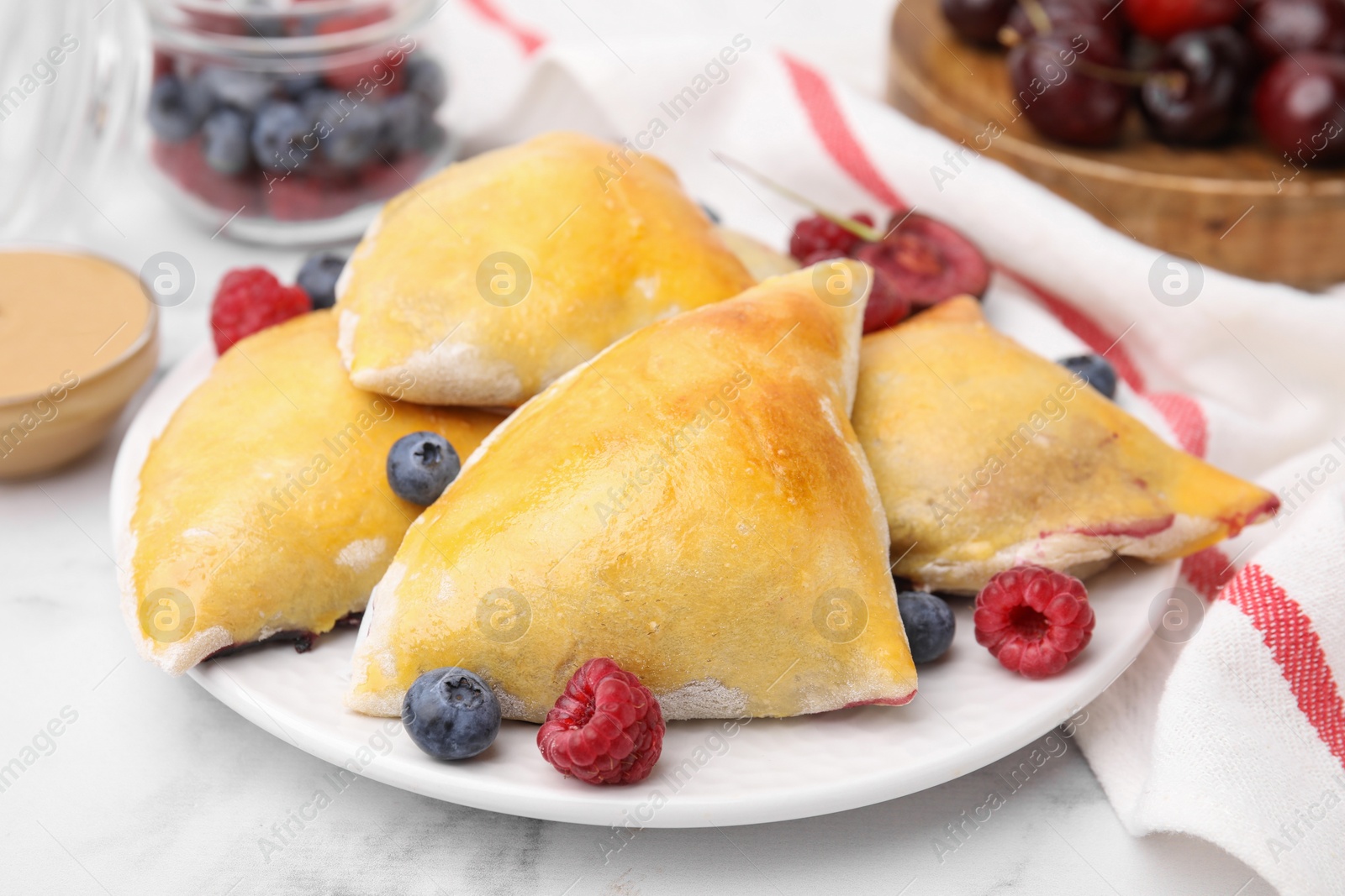 Photo of Delicious samosas with berries on white marble table, closeup