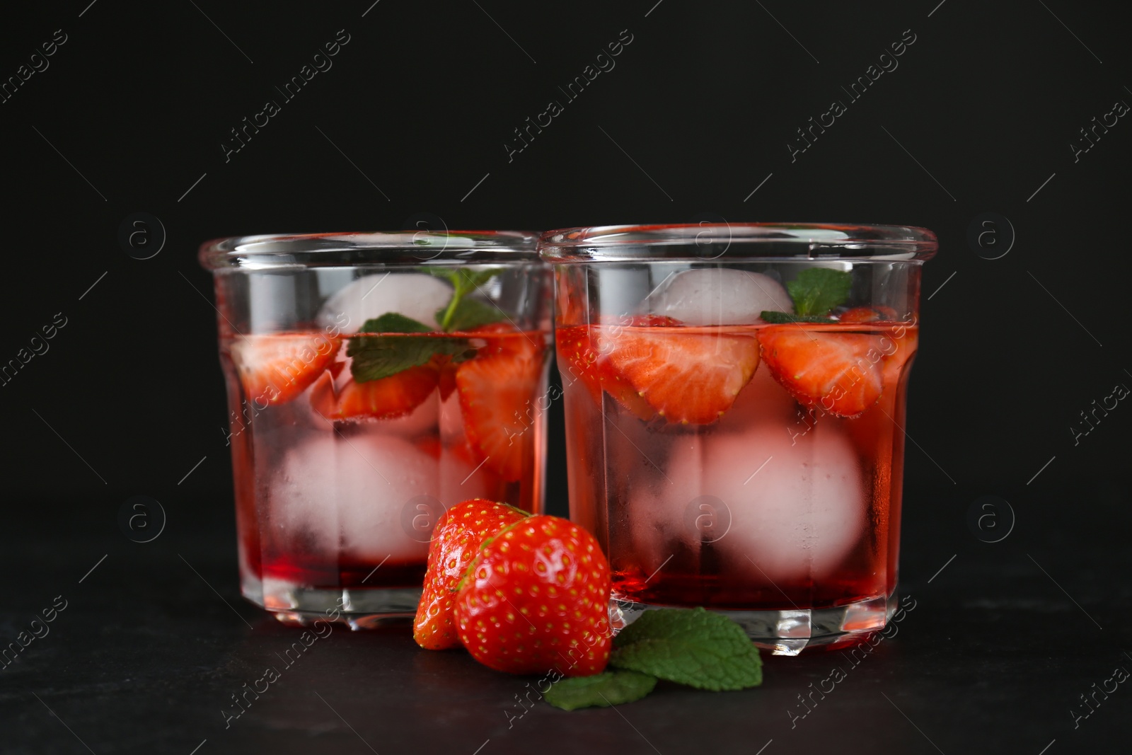 Photo of Delicious cocktails with strawberries, mint and ice balls on black table