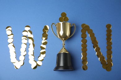 Photo of Gold trophy cup and word WIN made with confetti on blue background, flat lay