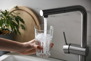 Photo of Woman filling glass with tap water from faucet in kitchen, closeup