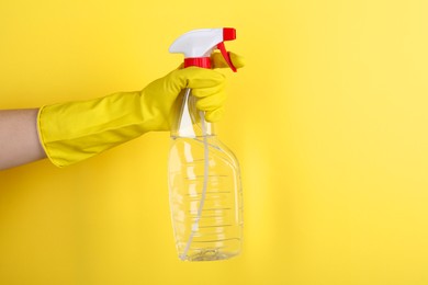 Woman holding plastic spray bottle on yellow background, closeup. Space for text