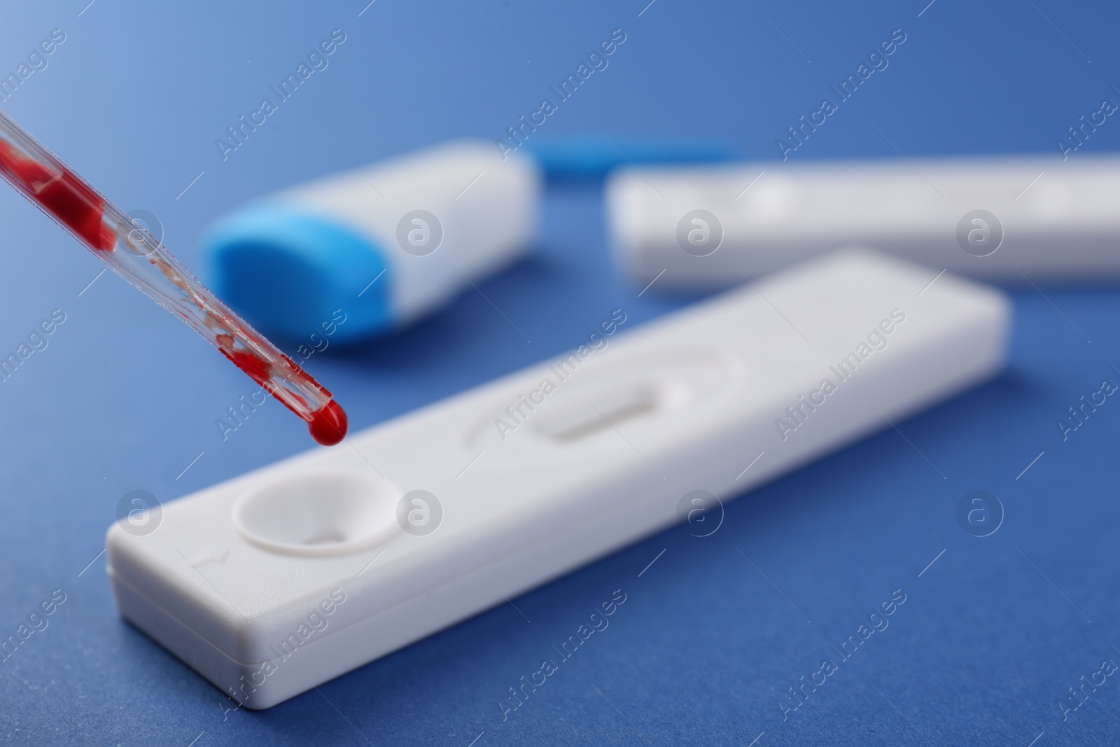 Photo of Dropping blood sample onto disposable express test cassette with pipette on blue background, closeup