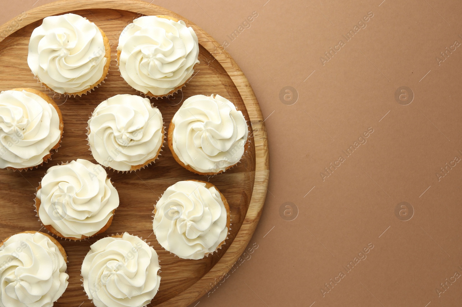 Photo of Tasty vanilla cupcakes with cream on dark beige background, top view. Space for text