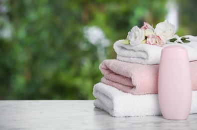 Soft towels, flowers and shower gel bottle on marble table outdoors, closeup. Space for text