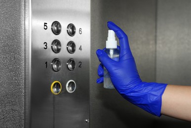 Photo of Woman cleaning buttons panel in elevator with detergent spray, closeup