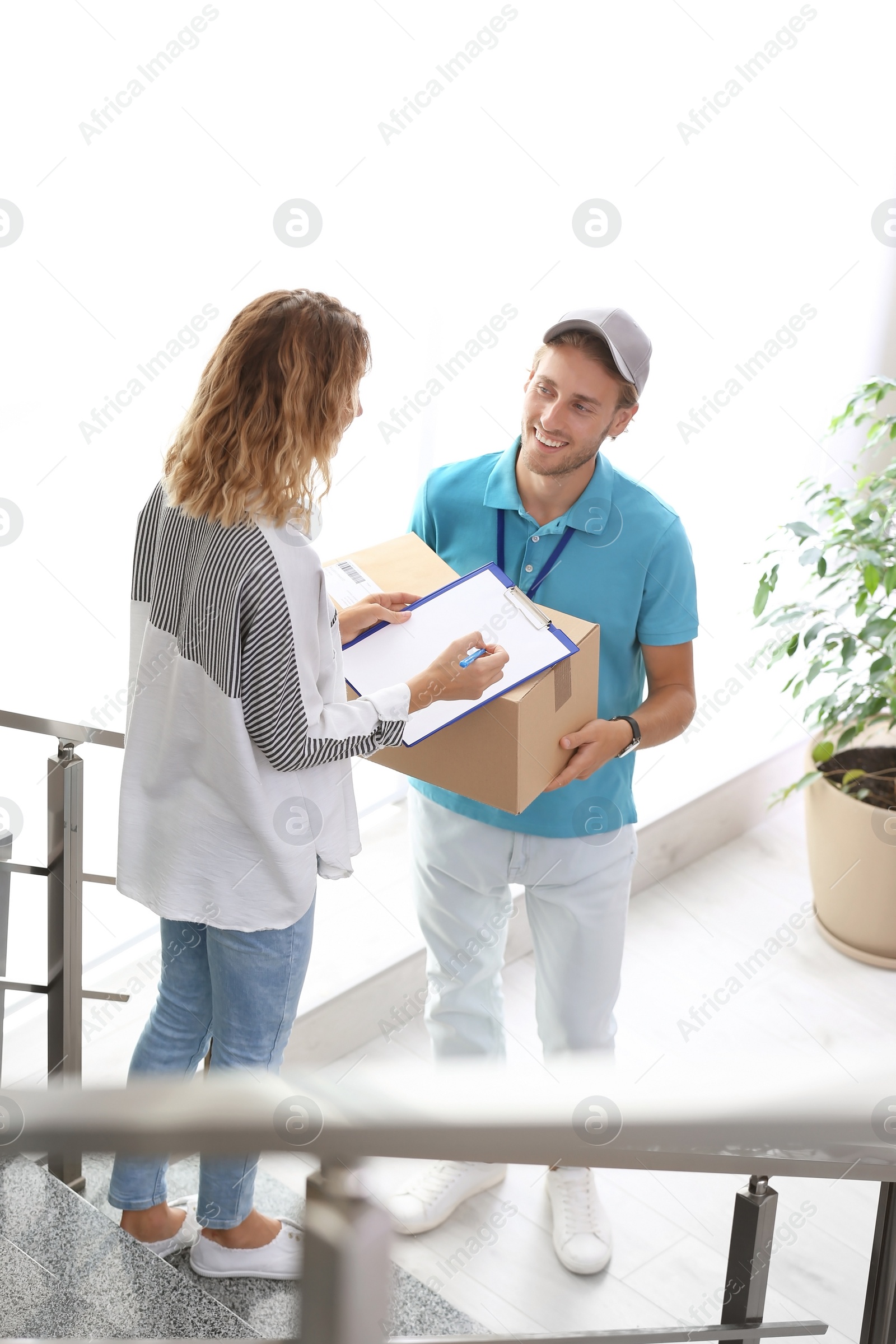 Photo of Young woman signing documents after receiving parcels from courier indoors