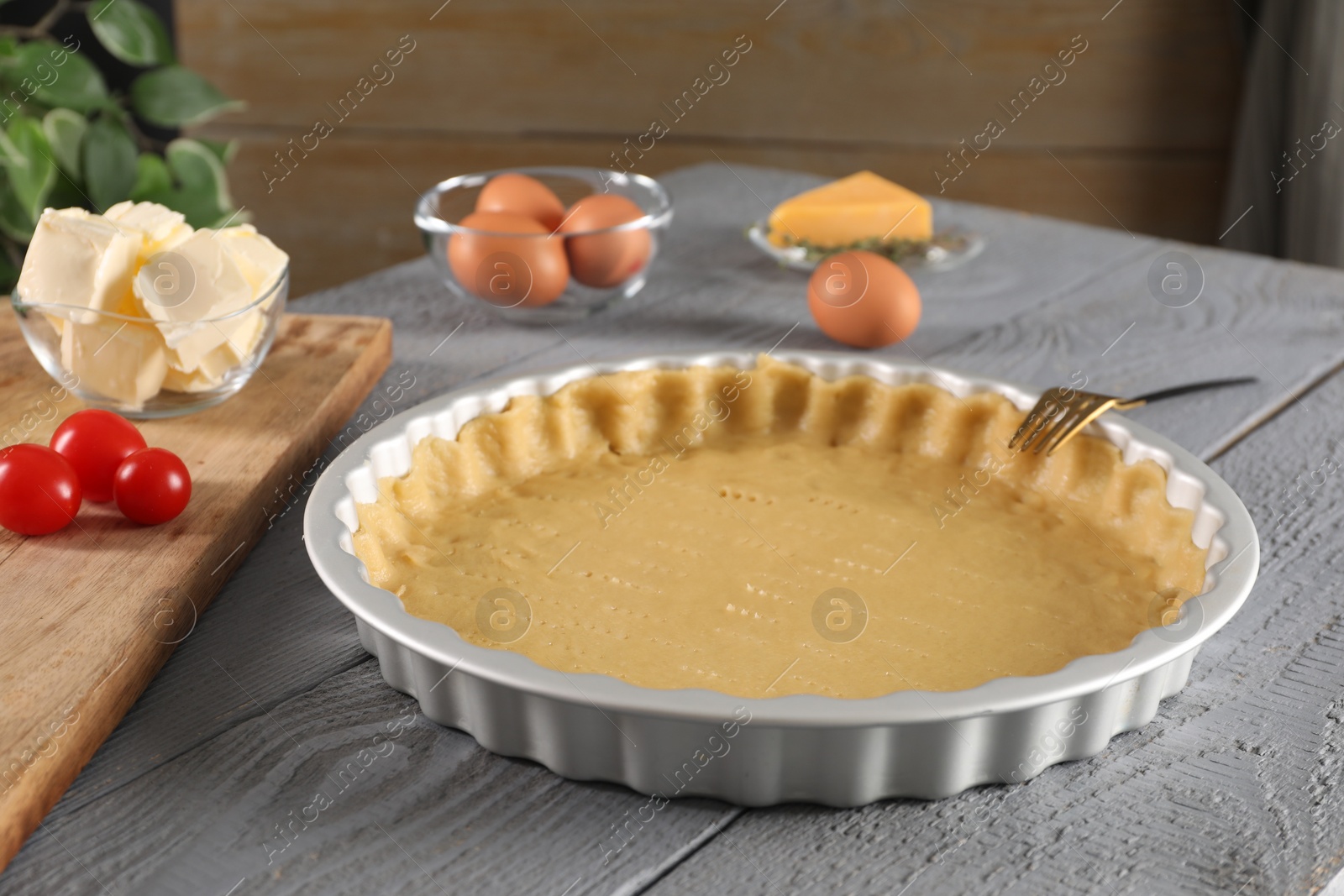 Photo of Making quiche. Baking dish with fresh dough and ingredients on grey wooden table.