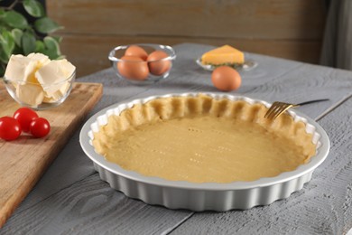 Making quiche. Baking dish with fresh dough and ingredients on grey wooden table.