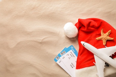 Airline tickets, Santa hat, toy airplane, starfish and space for text on beach sand, flat lay. Christmas vacation