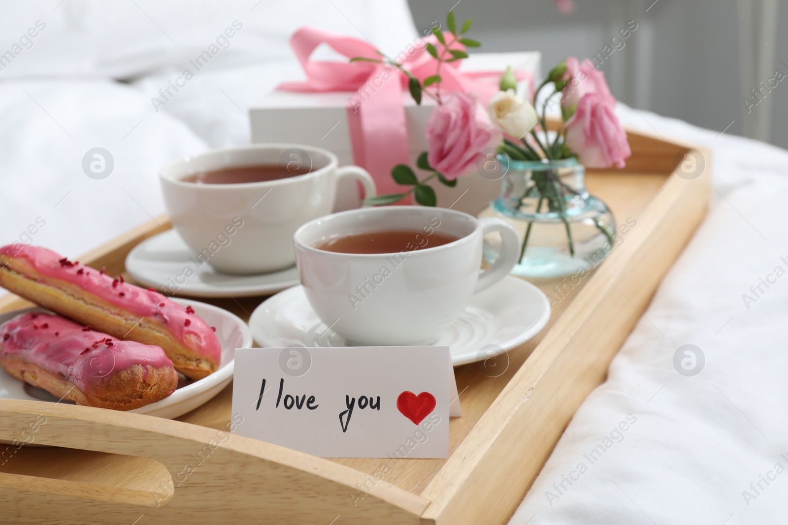 Photo of Tasty breakfast served in bed. Delicious eclairs, tea, gift box, flowers and card with phrase I Love You on tray