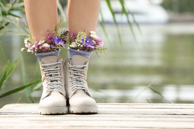 Photo of Woman standing on wooden pier with flowers in socks outdoors, closeup. Space for text