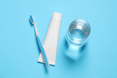 Photo of Plastic toothbrush with paste and glass of water on light blue background, flat lay