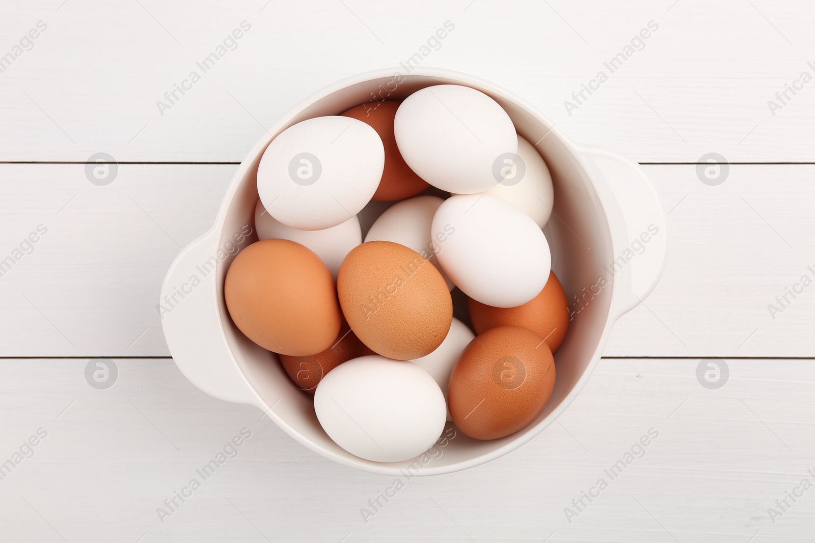 Photo of Unpeeled boiled eggs in saucepan on white wooden table, top view