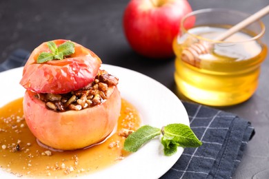 Photo of Tasty baked apple with nuts, honey and mint on gray table, closeup