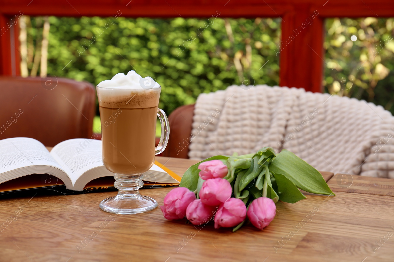 Photo of Glass of delicious cocoa, pink tulips and book on wooden table at terrace