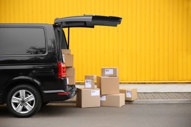 Photo of Black delivery van and many different parcels near yellow building outdoors, space for text. Courier service