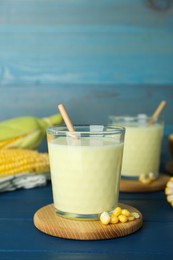 Photo of Tasty fresh corn milk in glasses and cobs on blue wooden table