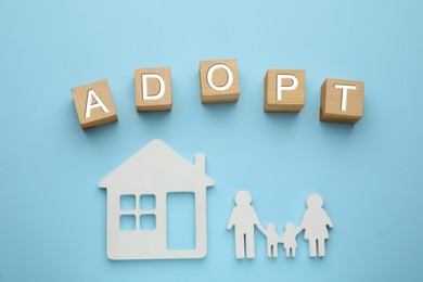 Photo of Family figure, house and word Adopt made of cubes on light blue background, flat lay