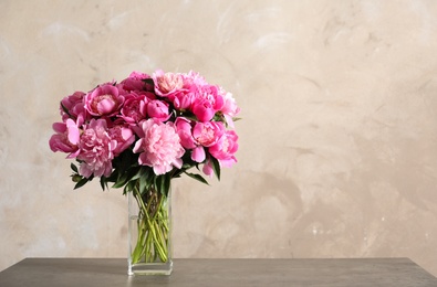 Photo of Fragrant peonies in vase on table against color background, space for text. Beautiful spring flowers