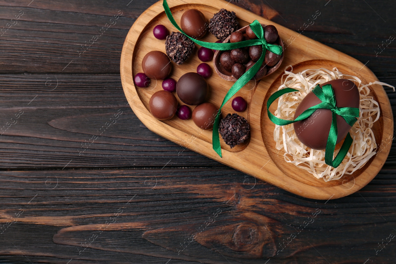 Photo of Tasty chocolate eggs with green bows and sweets on wooden table, top view