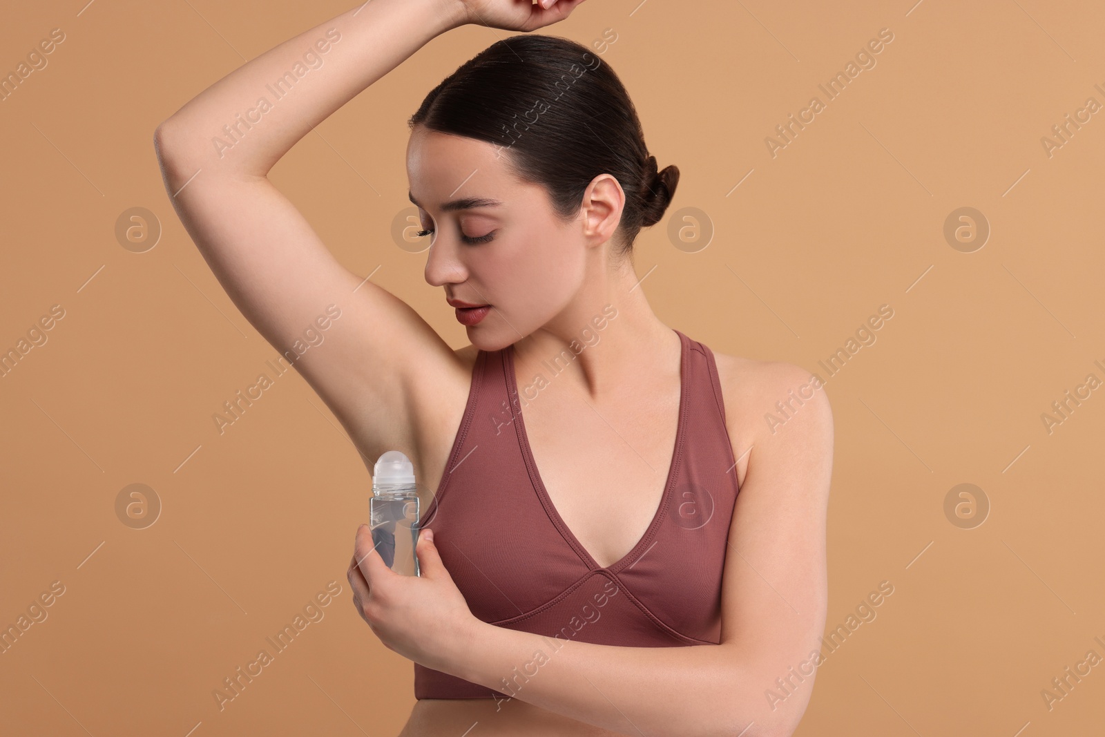 Photo of Beautiful woman applying deodorant on beige background