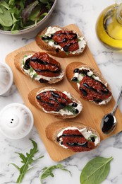 Photo of Delicious bruschettas with sun-dried tomatoes, cream cheese, balsamic vinegar and ingredients on white marble table, flat lay