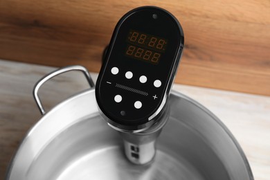 Photo of Sous vide cooker in pot on white wooden table, closeup. Thermal immersion circulator