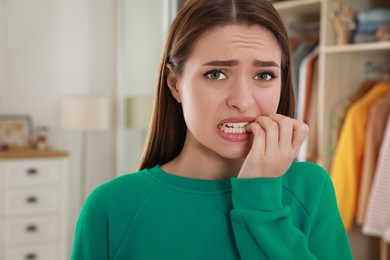 Photo of Young woman biting her nails at home