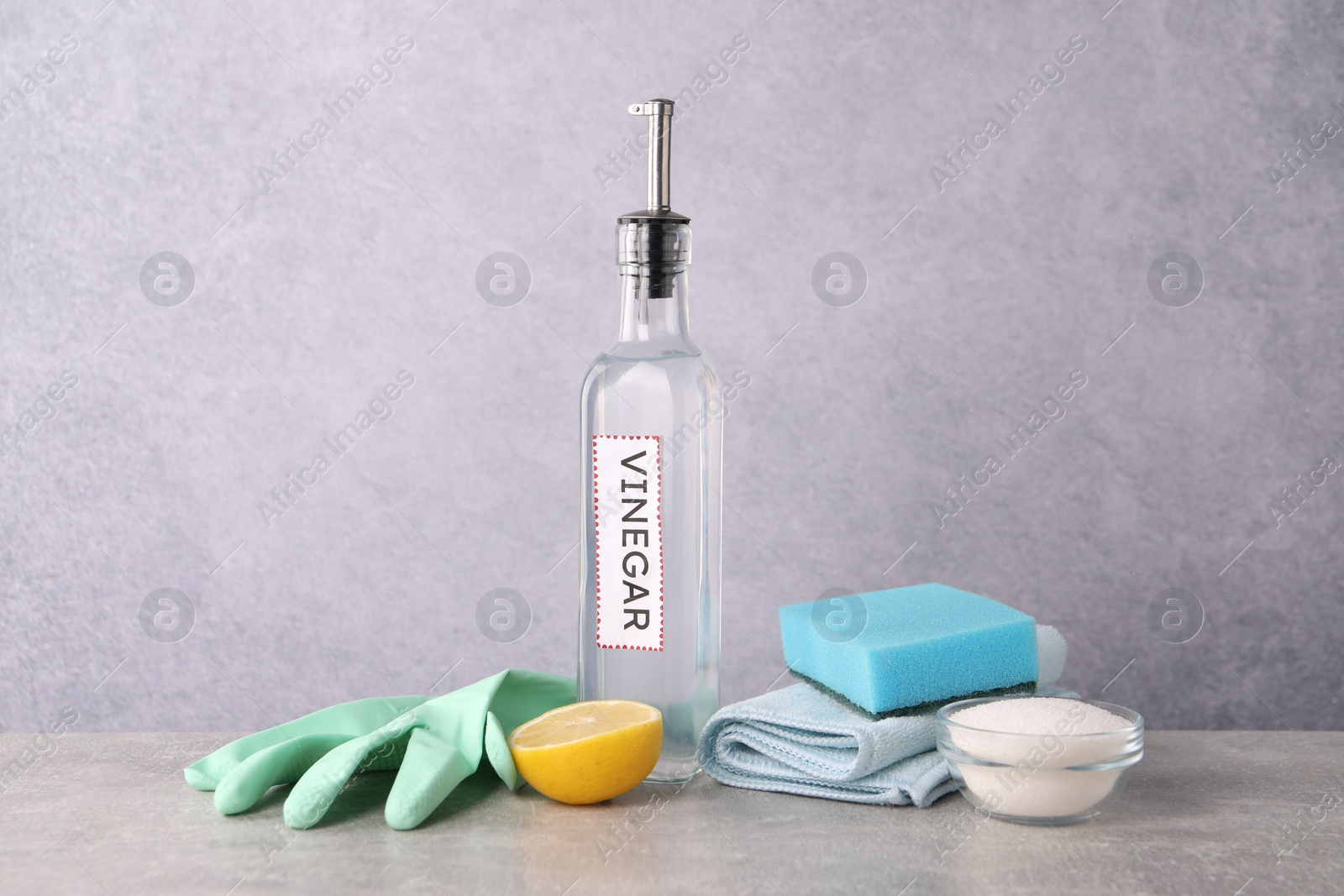 Photo of Natural cleaning products. Vinegar in bottle, baking soda, lemon, glove and sponge on light grey table