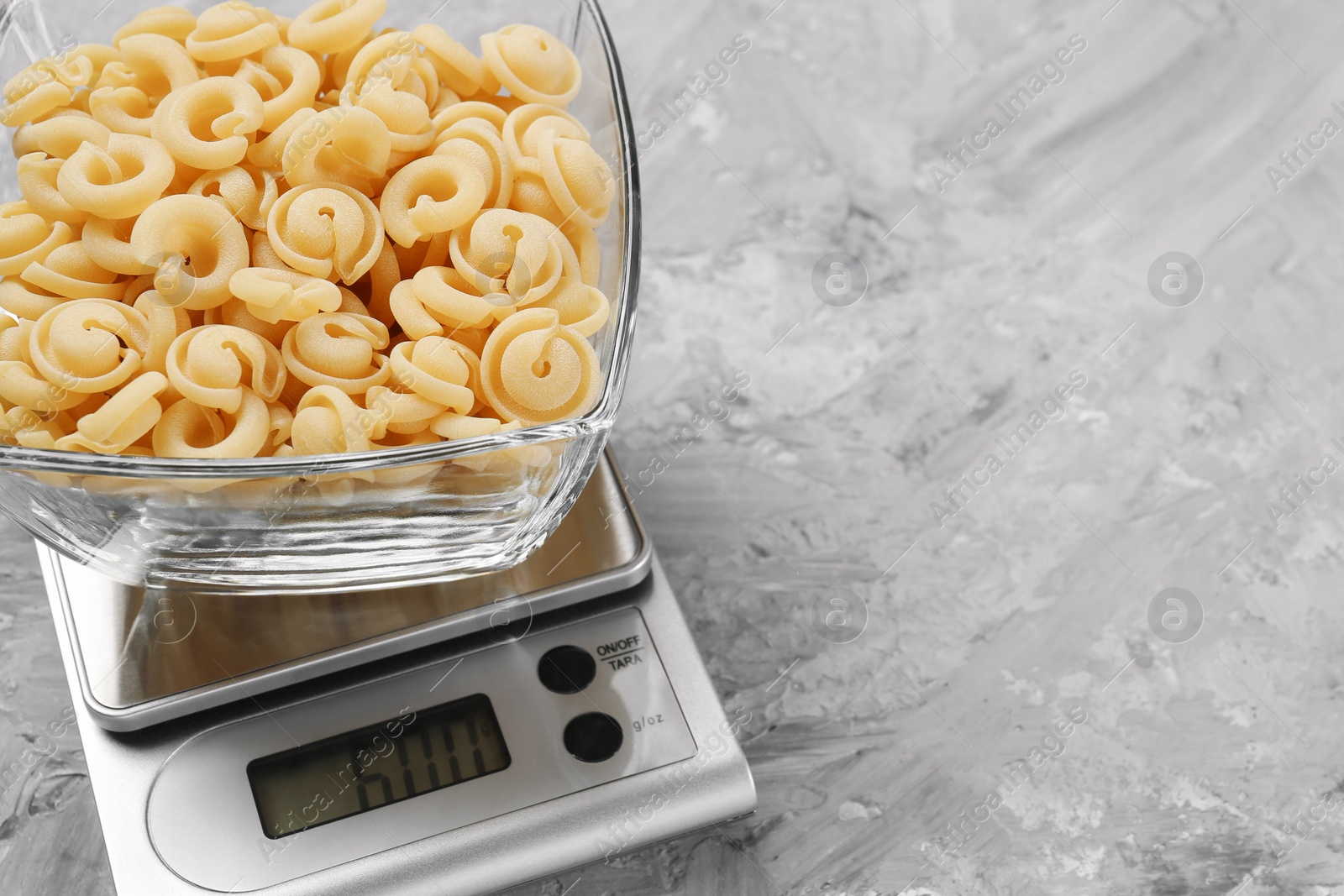 Photo of Kitchen scale with bowl of pasta on grey textured table. Space for text