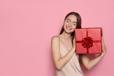 Portrait of happy young woman with gift box on pink background. Space for text