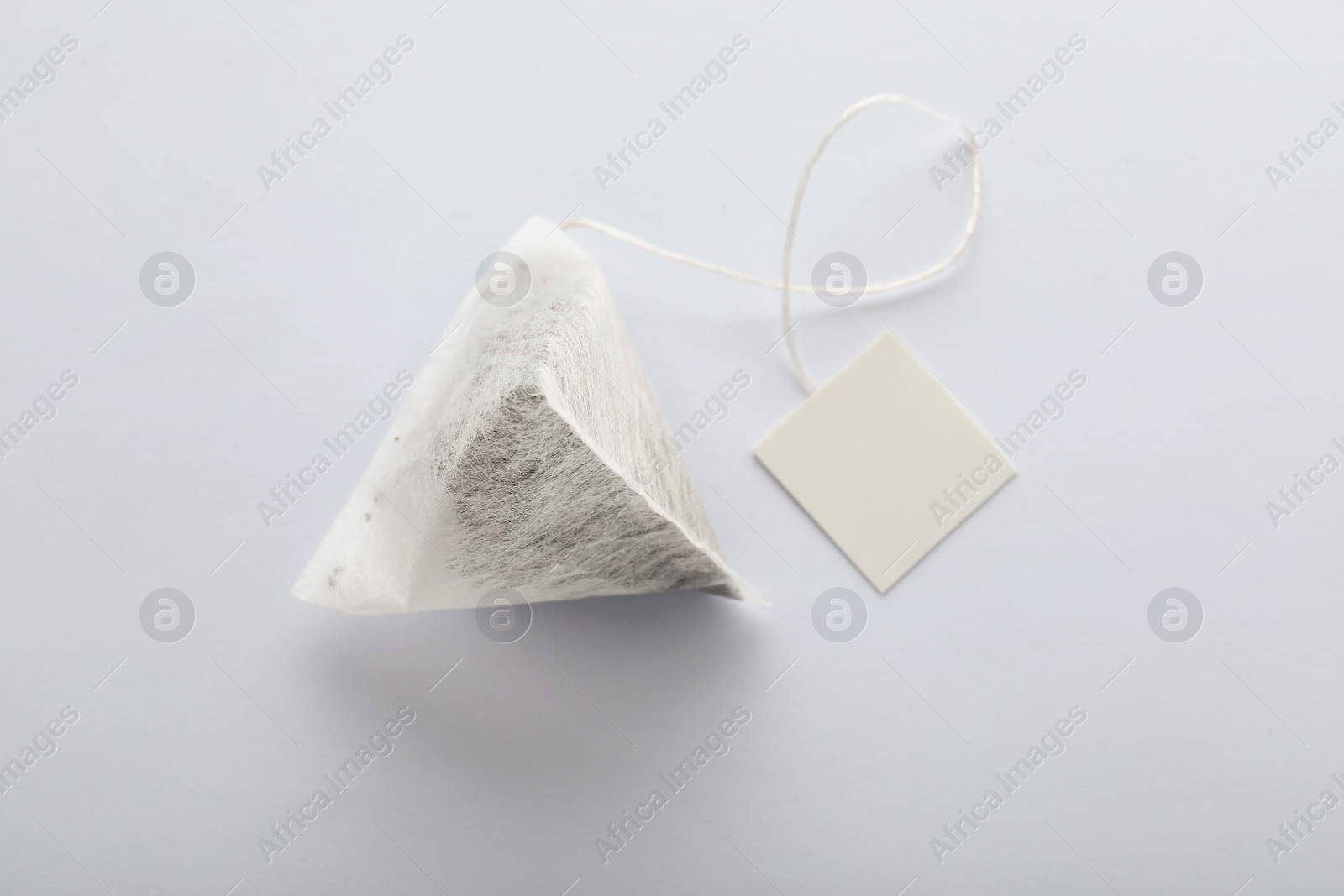 Photo of Unused pyramid tea bag with tag on white background, top view. Space for text