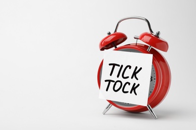 Photo of Alarm clock and sticky note with words TICK TOCK on white background. Time concept