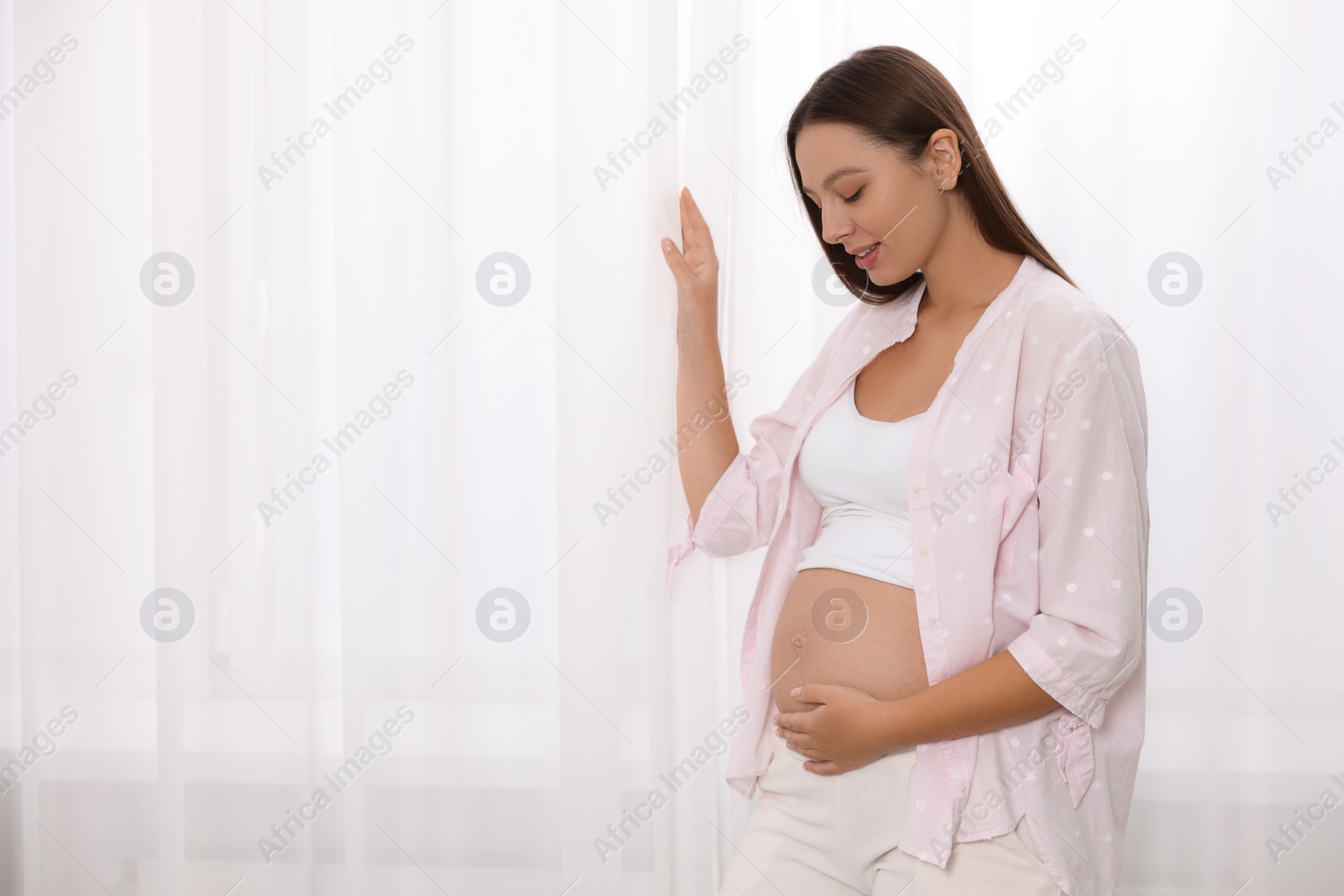 Photo of Beautiful pregnant woman near window indoors, space for text